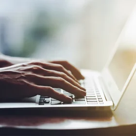手元でノートパソコンのキーボードを打ち込み明るい室内で作業している様子